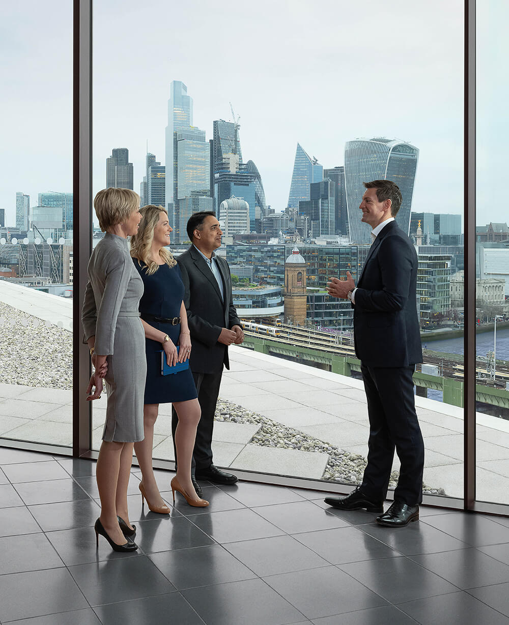 Four Baird associates conversing near a large window in the London office overlooking the London skyline