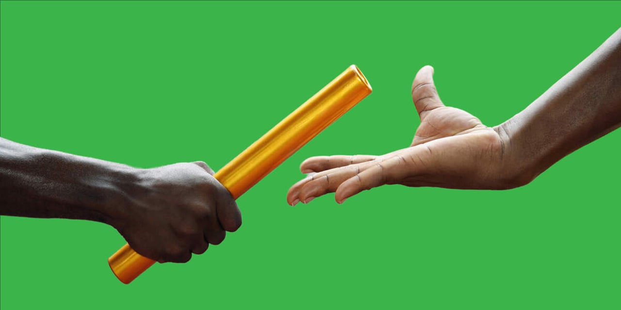 Photo of a baton being passed from one hand to another on a green background.