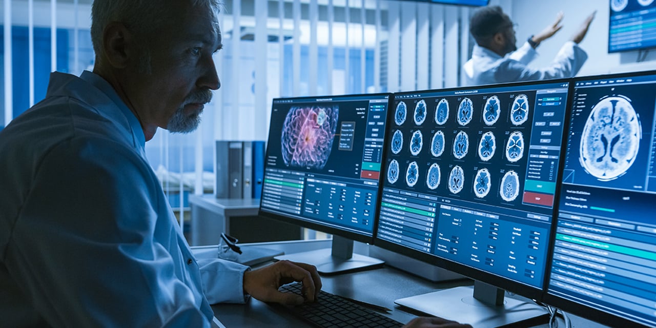 Doctor sitting in front of several computer monitors looking at a brain scan.