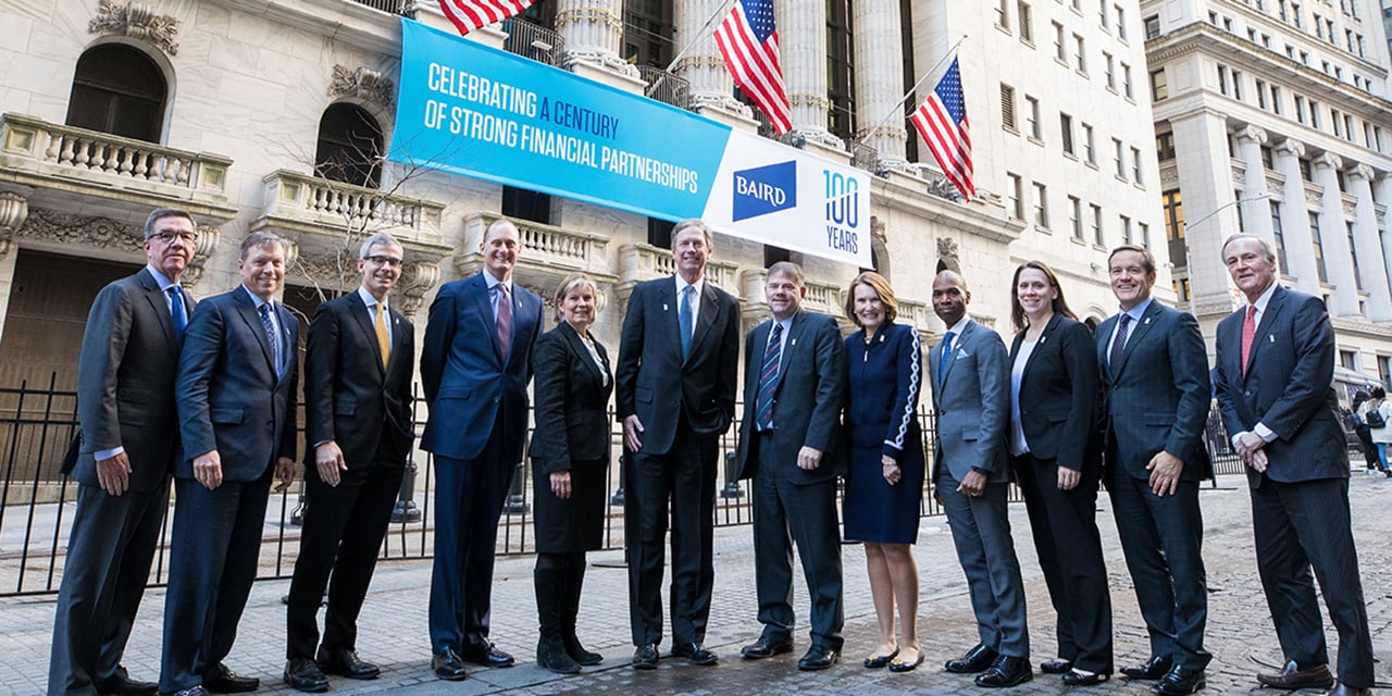 Baird leadership standing in front of the New York Stock Exchange with a banner celebrating Baird's 100th anniversary in the background.