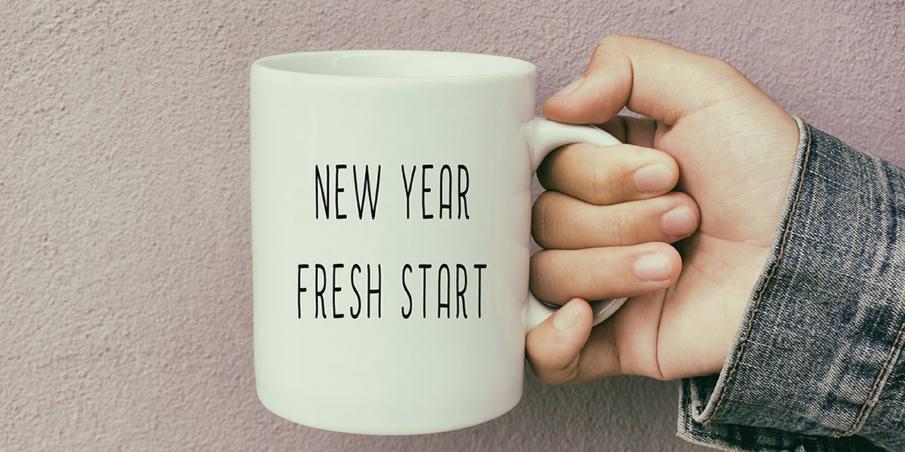 Hand holding a coffee mug with the words new year, fresh start printed on the cup.