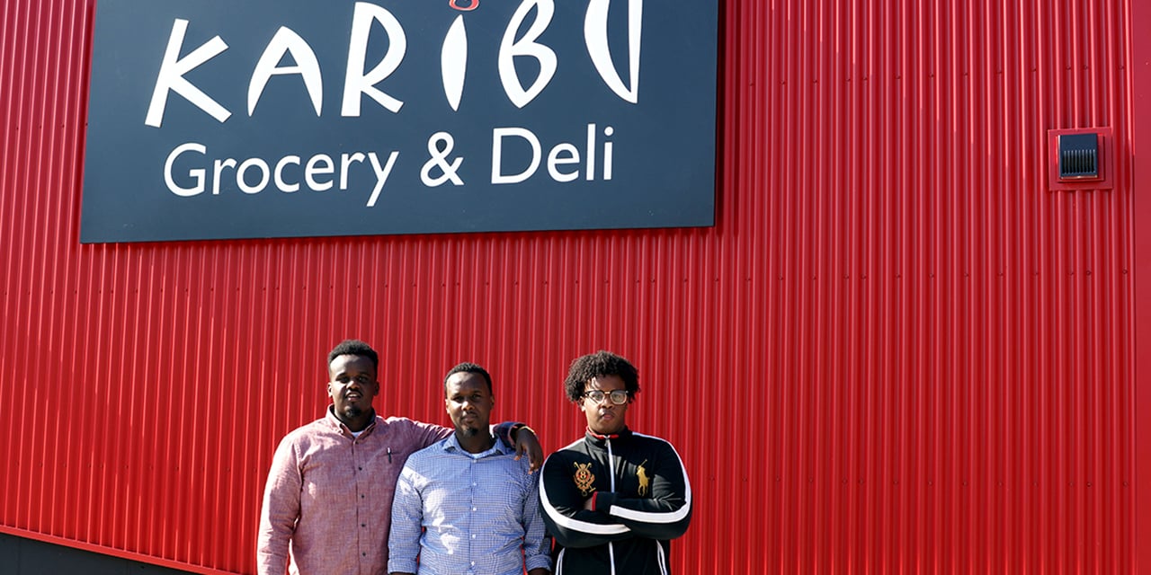 Photo of three men standing in front of the Karibu Grocery & Deli sign.