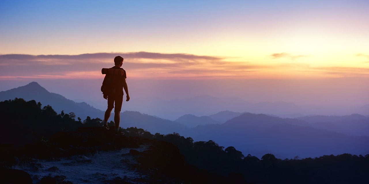 Hiker standing on a bluff at sunrise.
