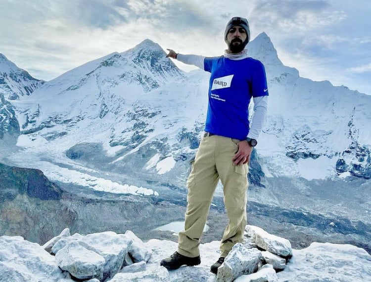 Karan Saberwal on points to mountain peaks behind him on his ascent of Mount Everest