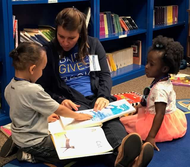 Baird associate reading a book to two children in a library.