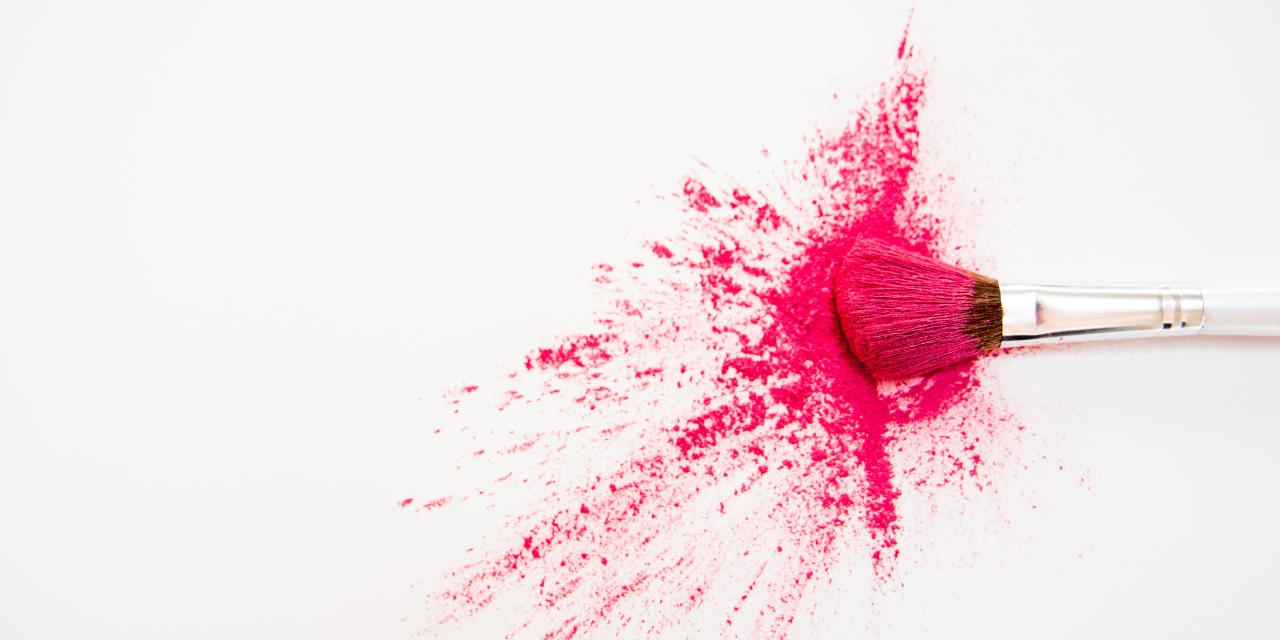 A makeup brush splattering red powder against a white background
