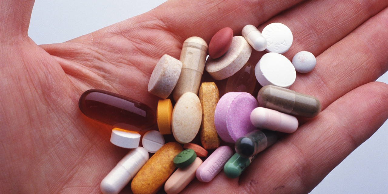 Hand holding a variety of supplement pills