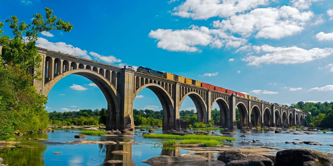 Train moving across elevated bridge over a river during the daytime.