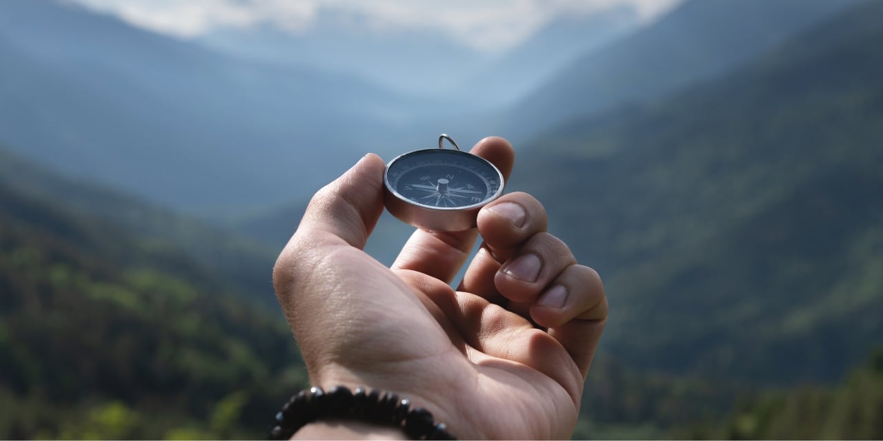 Hand holding a compass with mountains in the distant background.