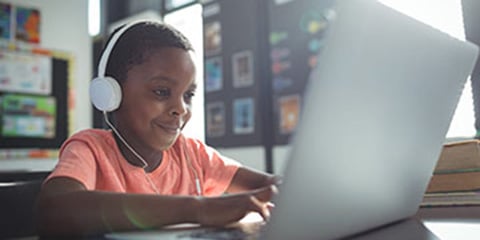 Elementary school aged child wearing headphones and working on a laptop.