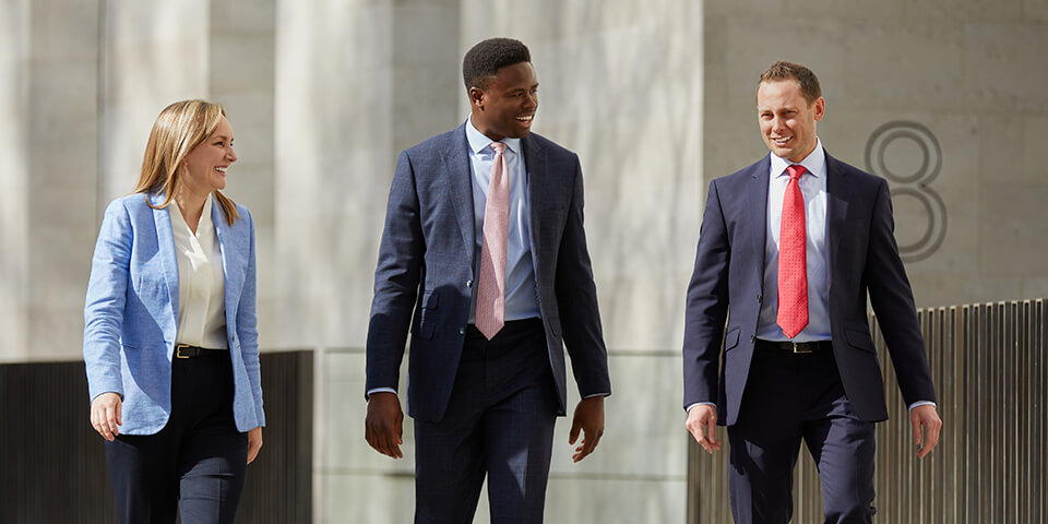 A candid photo of three Baird associates walking outside the office building on a sunny day