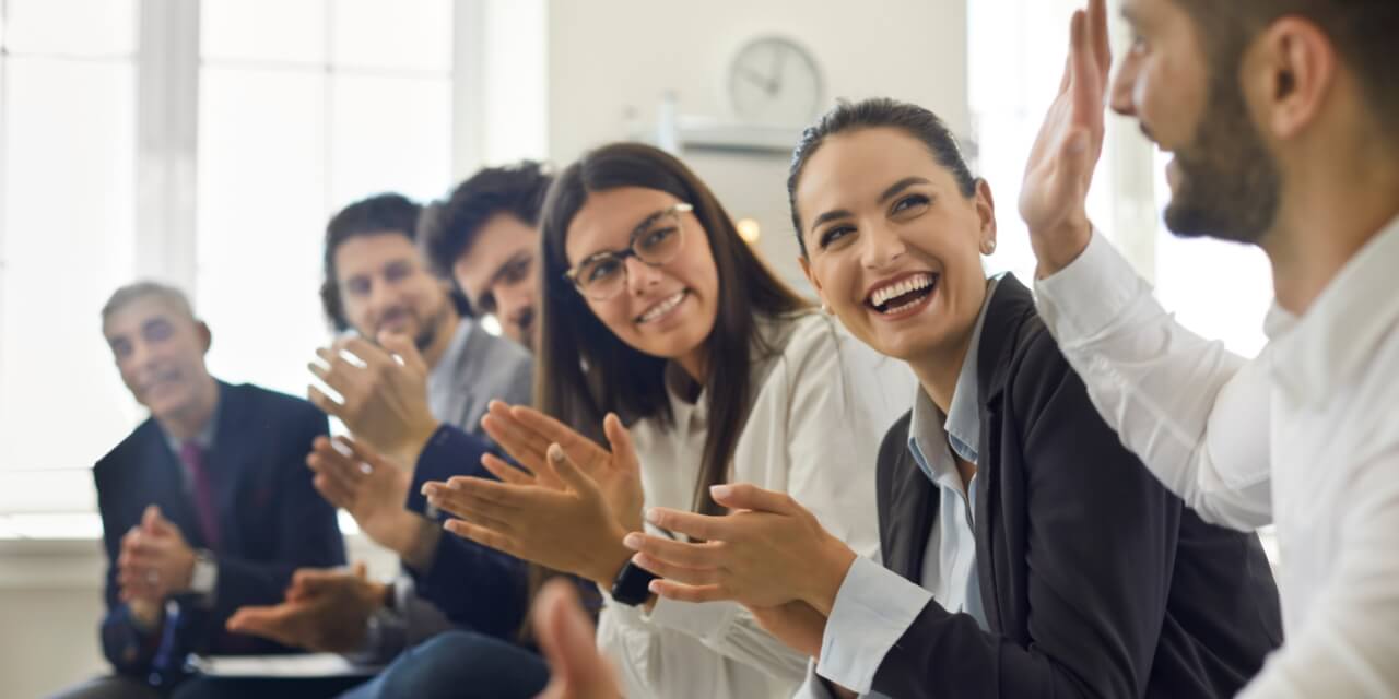 A group of people wearing business attire clapping and smiling