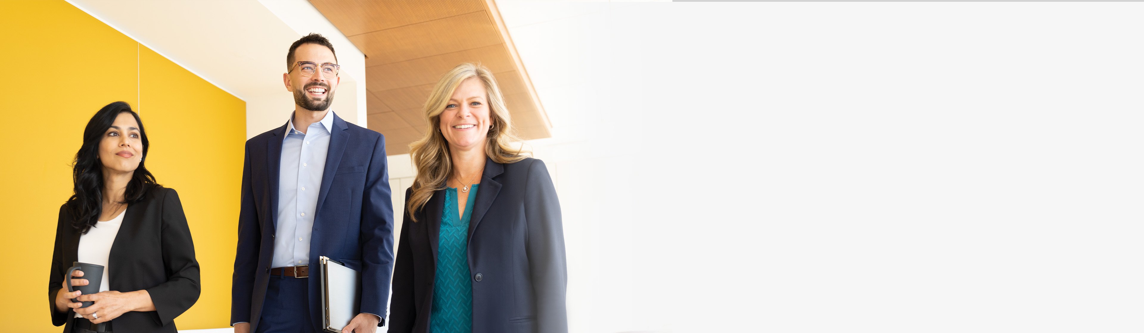 Three people stand in a brightly lit hallway with a yellow wall on the left