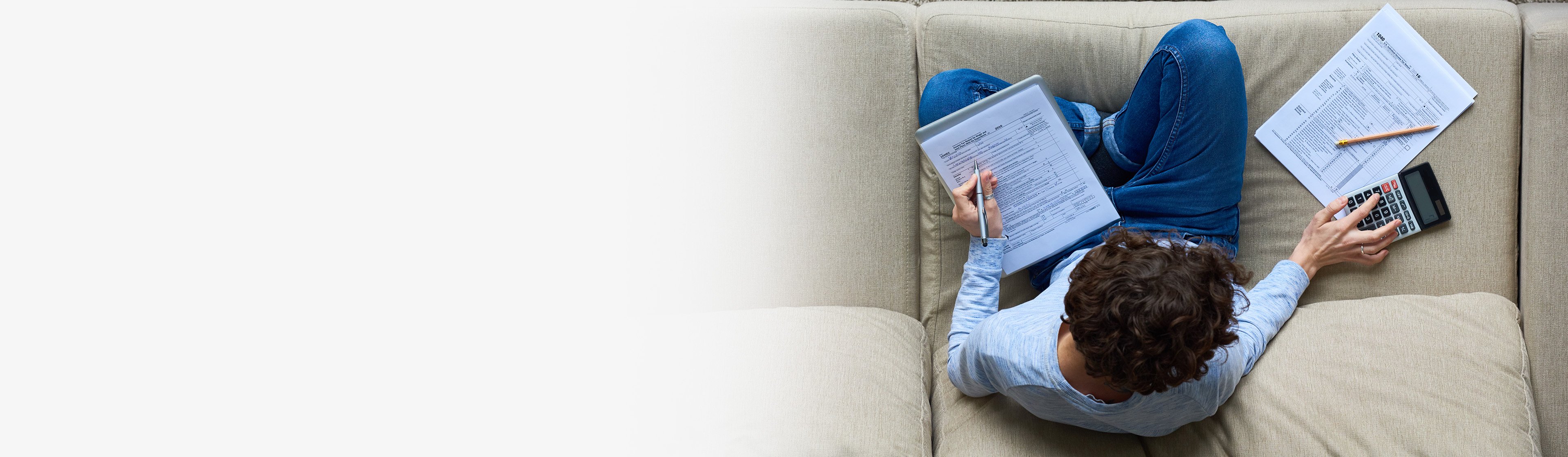 Overhead view of person reviewing financial documents with calculator and pen on a sofa