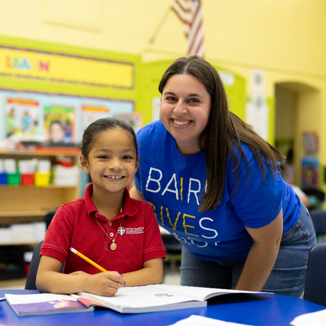 Warm classroom candid with clear volunteer activity.