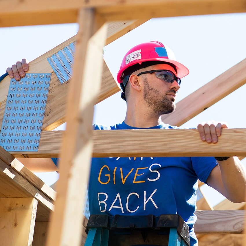 A man in a Baird Gives Back t-shirt holds roof rafters at a Habitat for Humanity volunteer event