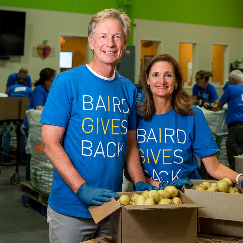 Steve Booth and a woman in a Baird Gives Back t-shirt are volunteering at a food bank.