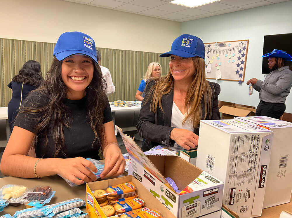 Two Baird associates wearing Baird Gives Back hats assemble snack bags at Seattle Homeless Outreach