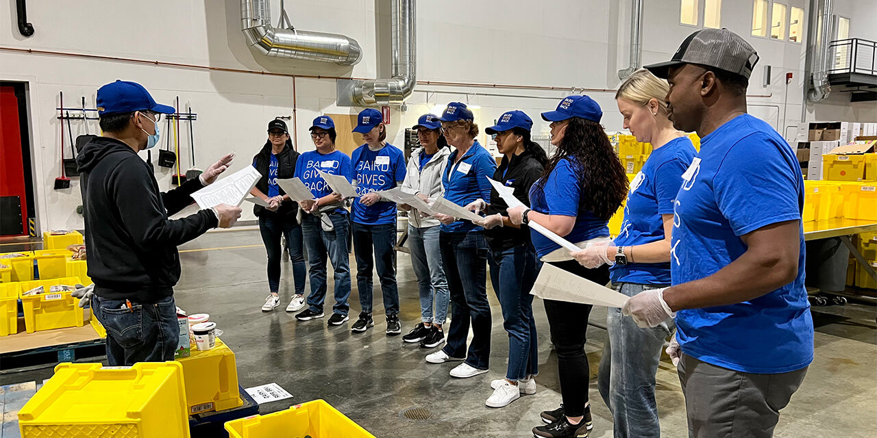 A group of Baird associates in Baird Gives Back t-shirts listen to instructions as they start a volunteer session at Food Lifeline in Seattle