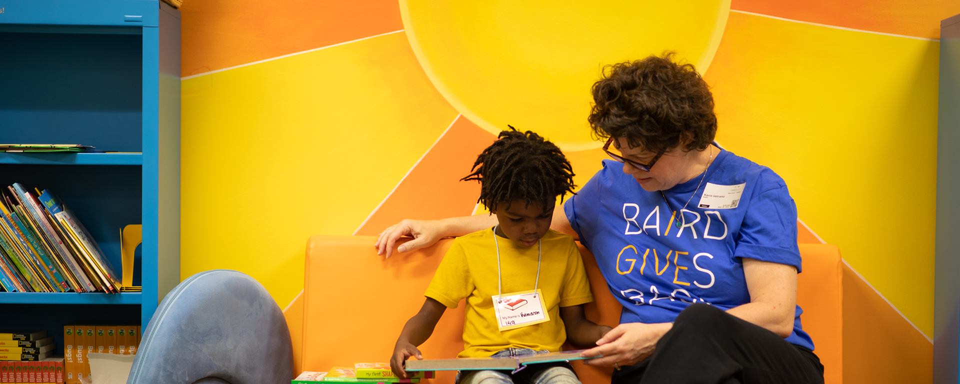 Woman in a Baird Cares t-shirt reading to a student.