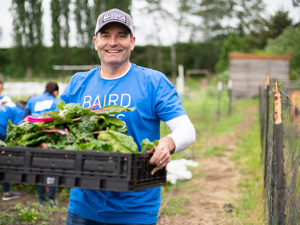 Male Baird Associate carrying harvested greens during Baird Gives Back week.