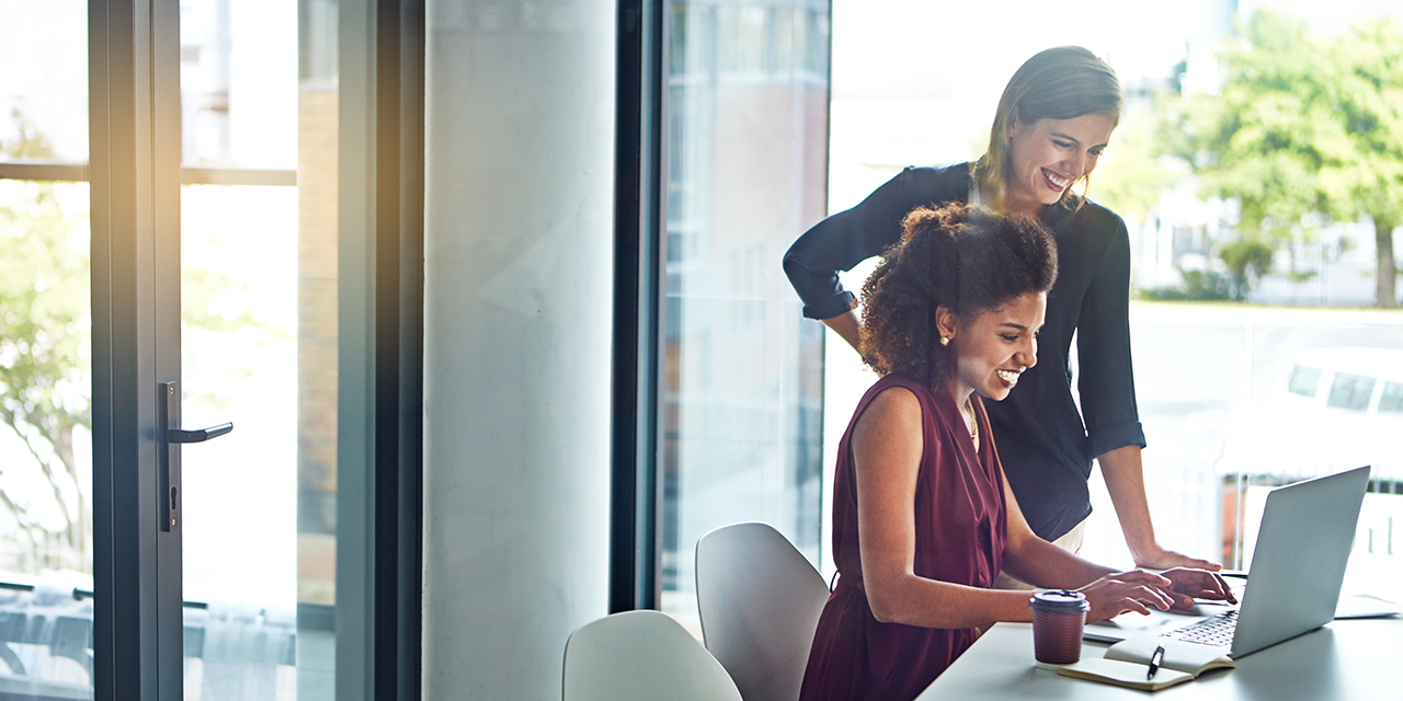 Two professional women working at a conference table looking at a laptop.