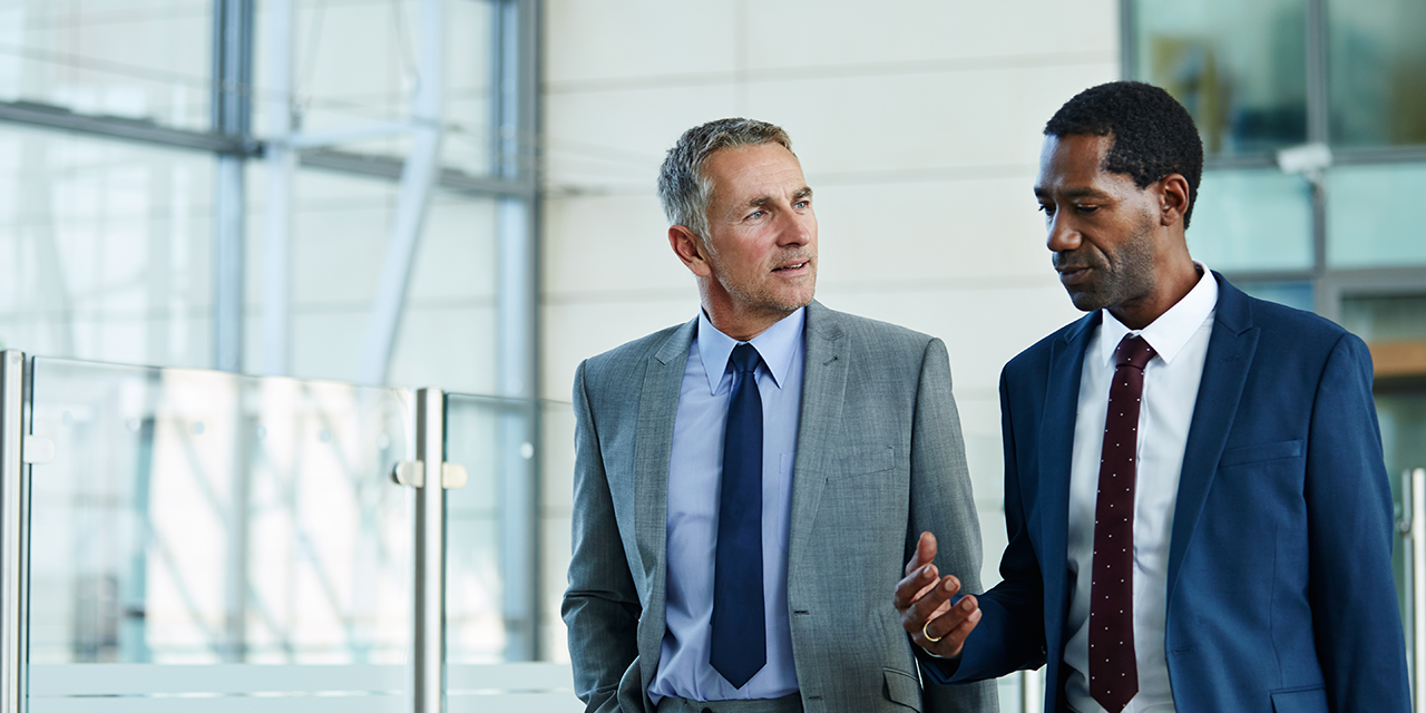 Two professionally dressed men talking while walking in a building