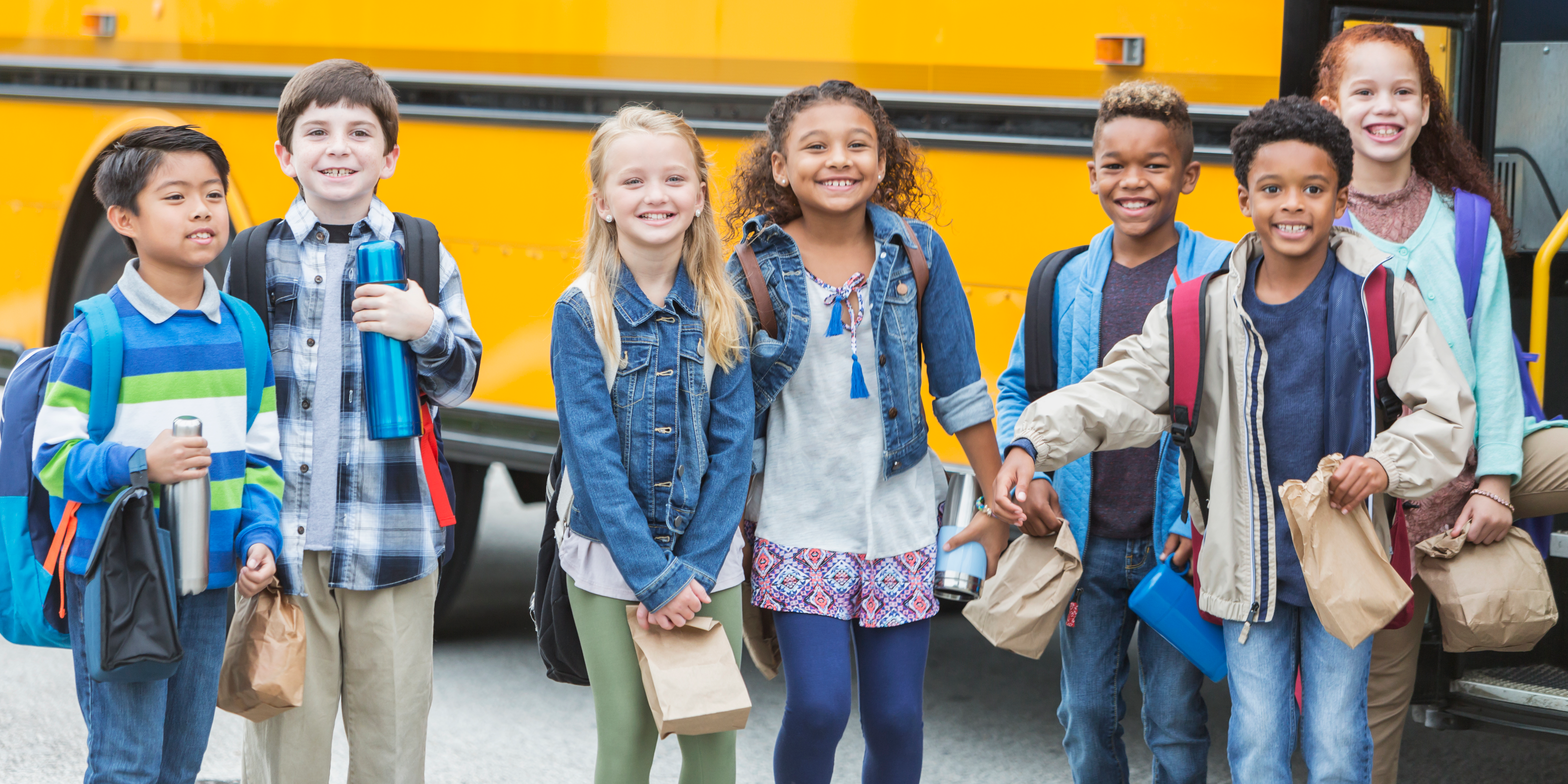 Elementary school children standing in front of a bus.