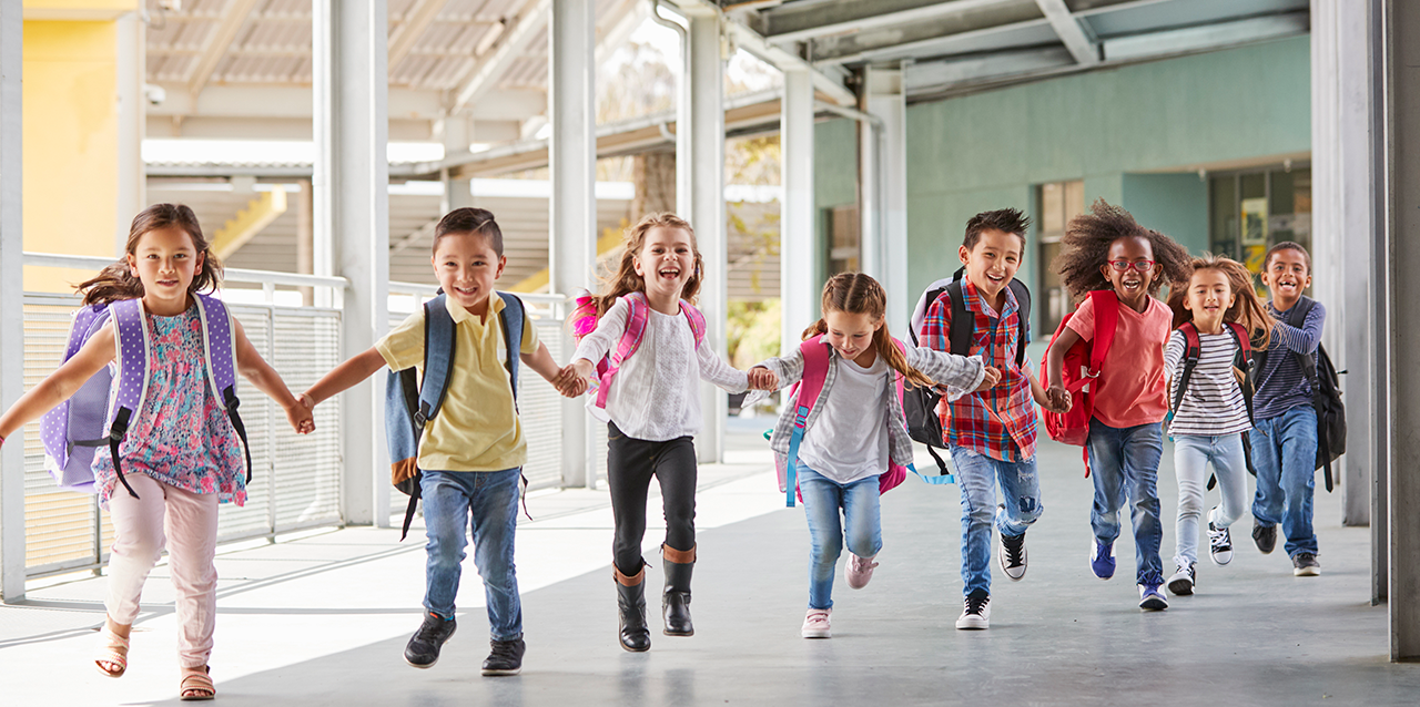 Elementary school children holding hands while walking down a school hallway.