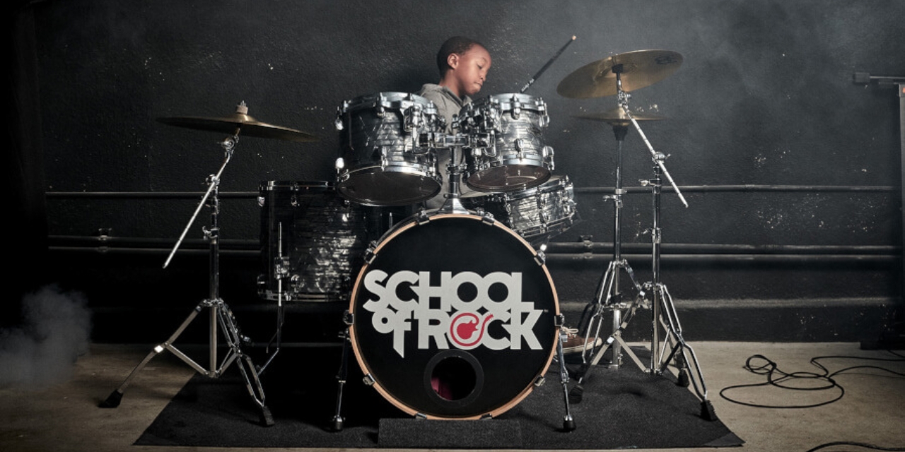 Young boy playing the drums. Bass drum includes School of Rock logo.