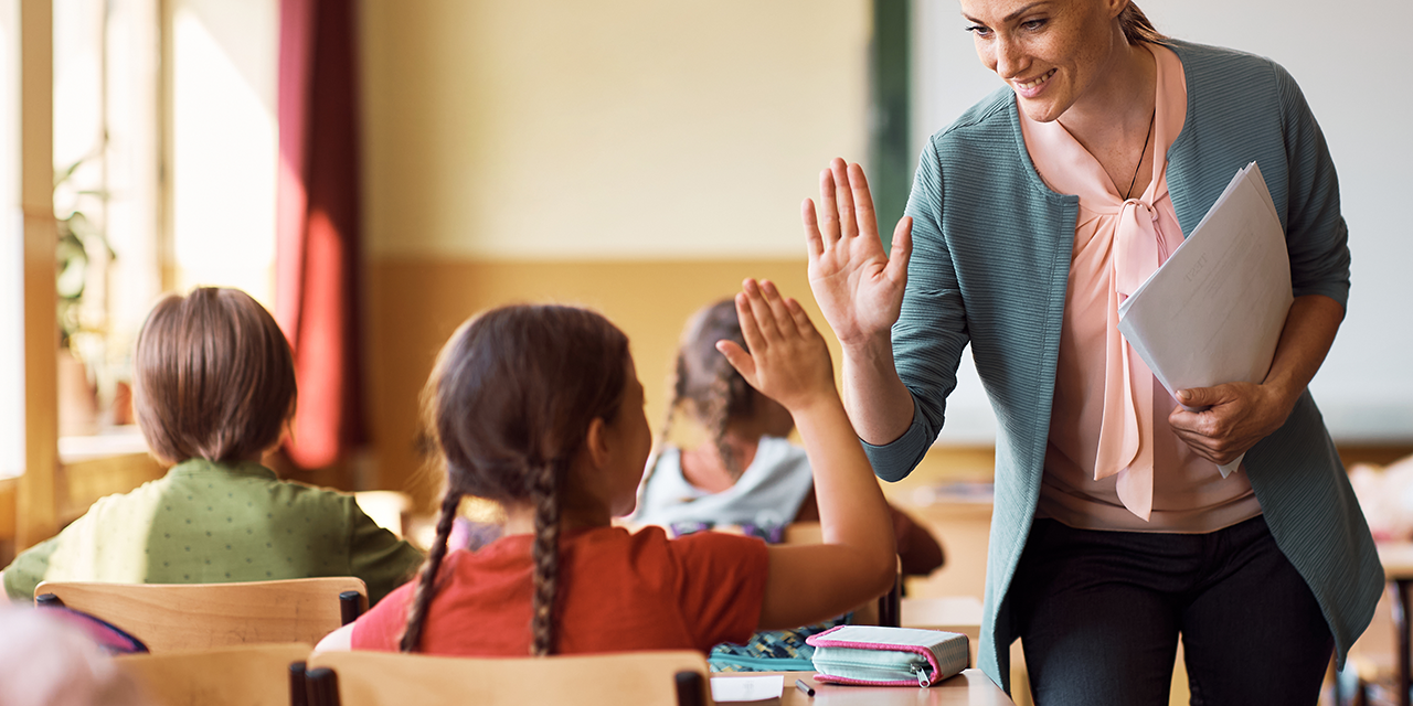 Teaching giving an elementary school student a high five in a classroom