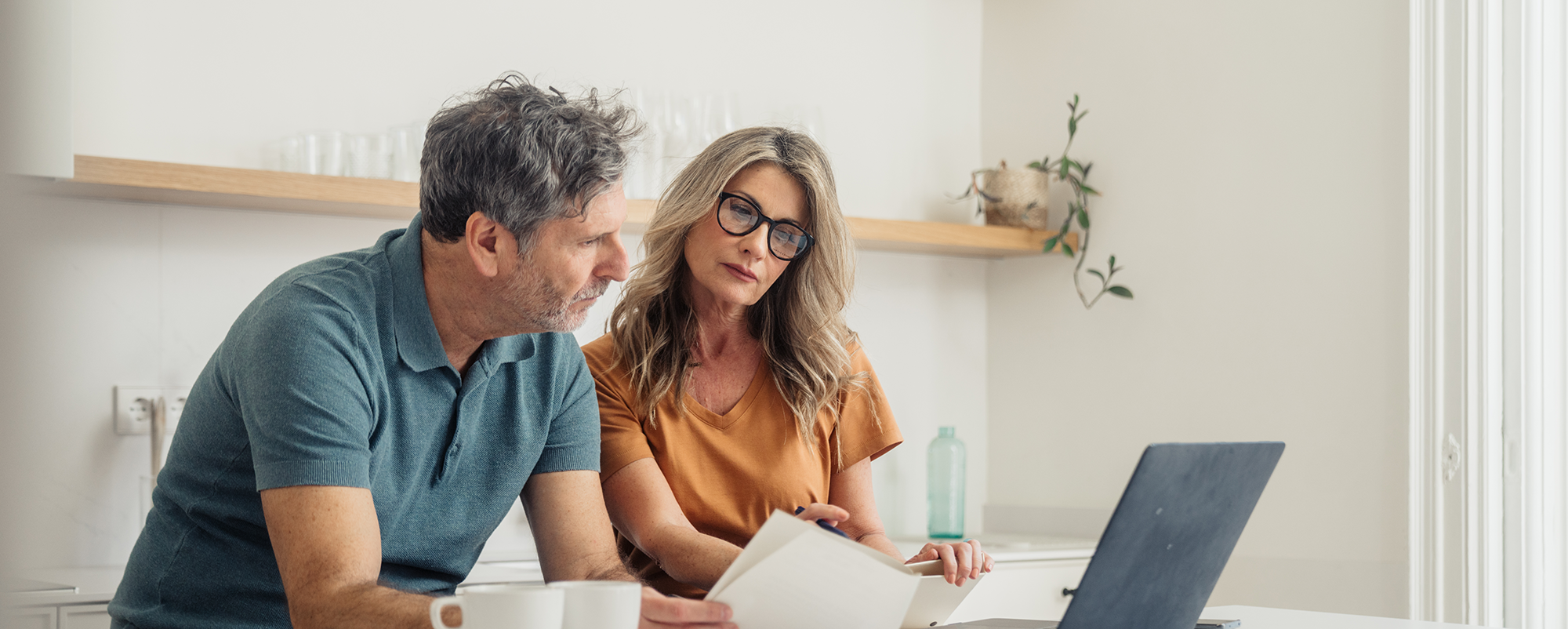Two people sitting at a table, reviewing papers with a laptop open nearby.