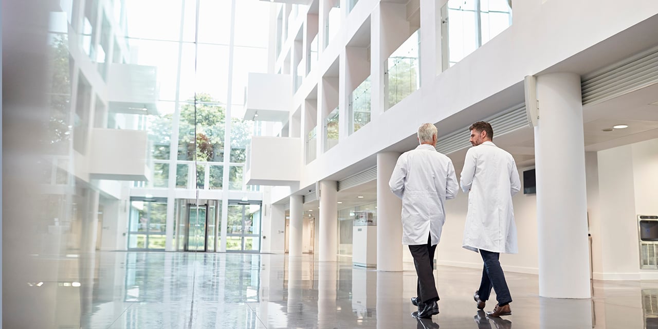 Two people in lab coats walking through a building hallway during the day