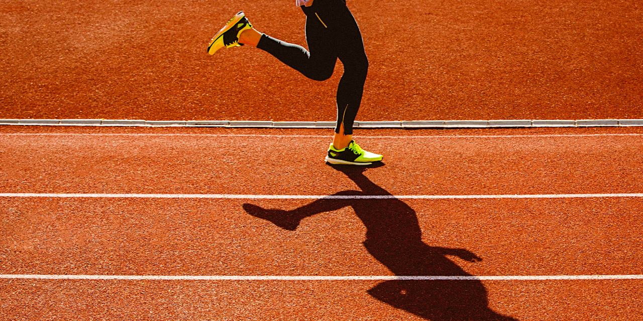 Person wearing yellow and black track shoes running on an orange track