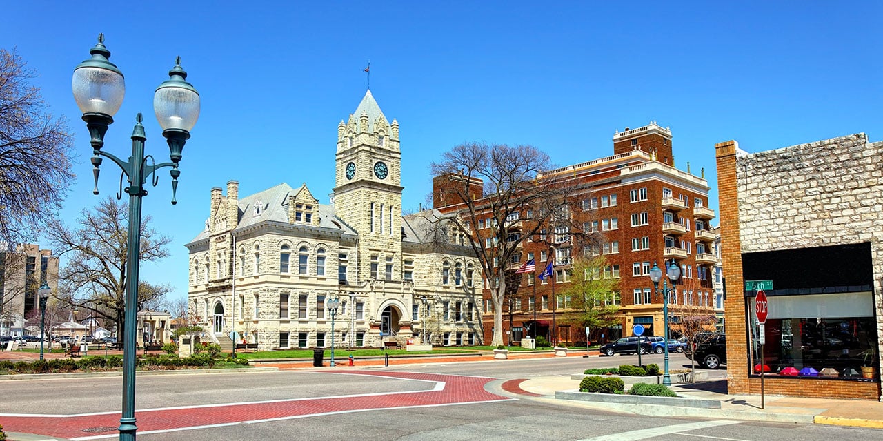 Historic stone courthouse with clock tower on a sunny day, surrounded by street and nearby buildings.