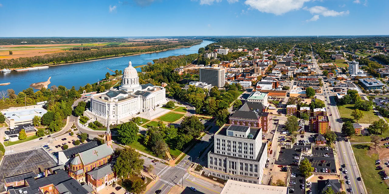 Aerial view of a city with a white-domed capitol building, river, and surrounding downtown buildings.