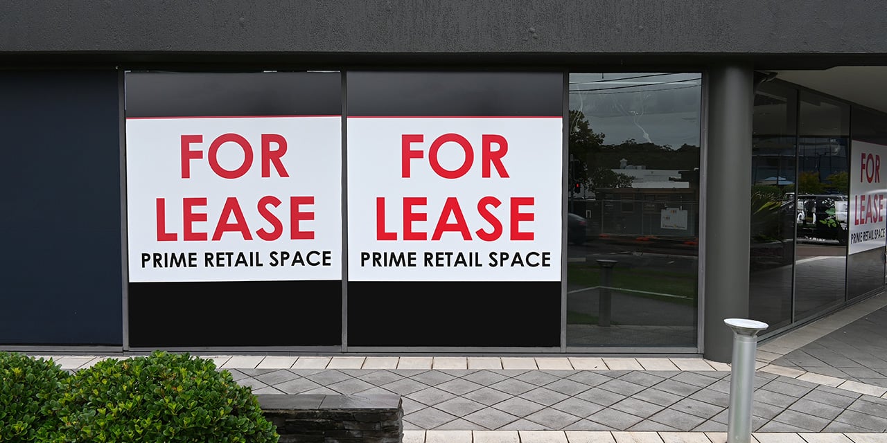 Exterior photo of a commercial building with two large signs in the window that read, 'For Lease - Prime Retail Space'