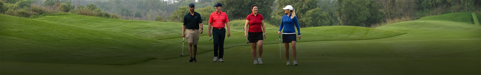 Four people in golf attire engaged in conversation while walking on a golf course