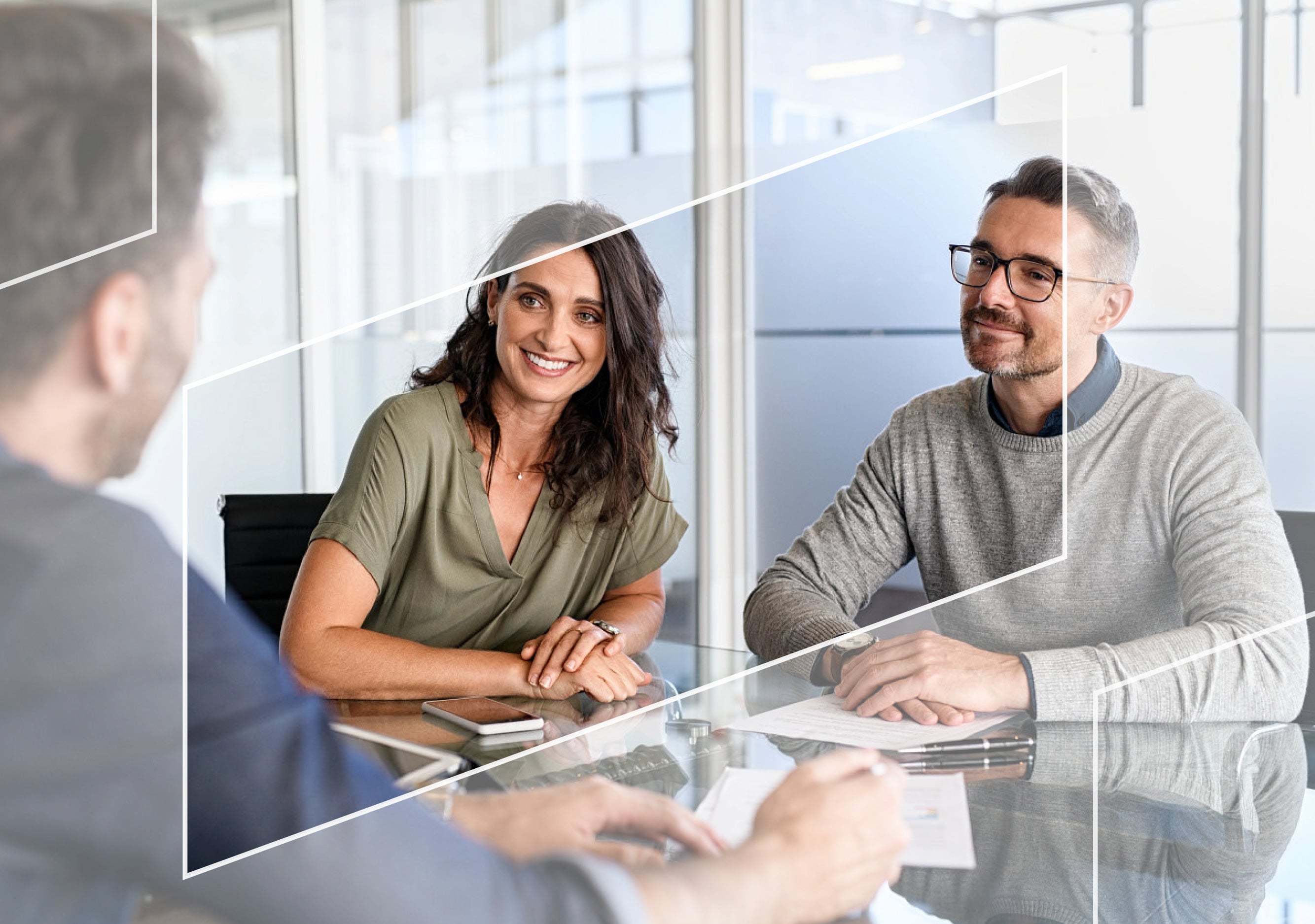 Clients meet with advisor reviewing documents at desk in a modern office, framed by parallelogram shapes