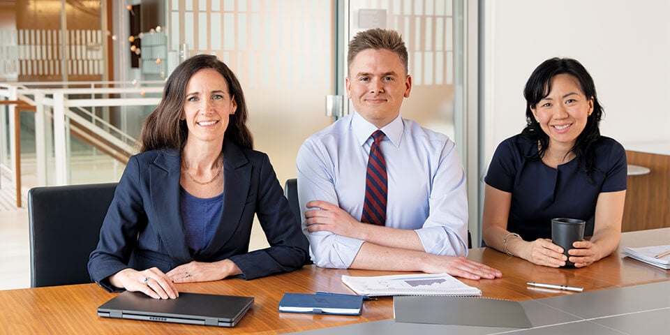 An image of three associates smiling as they meet in a conference room