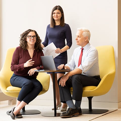 An image of three Principal Investments associates excitedly talking around a computer