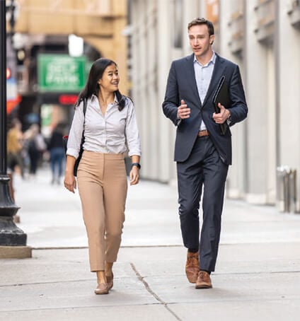 Candid photo of two associates conversing as they walk down a sidewalk