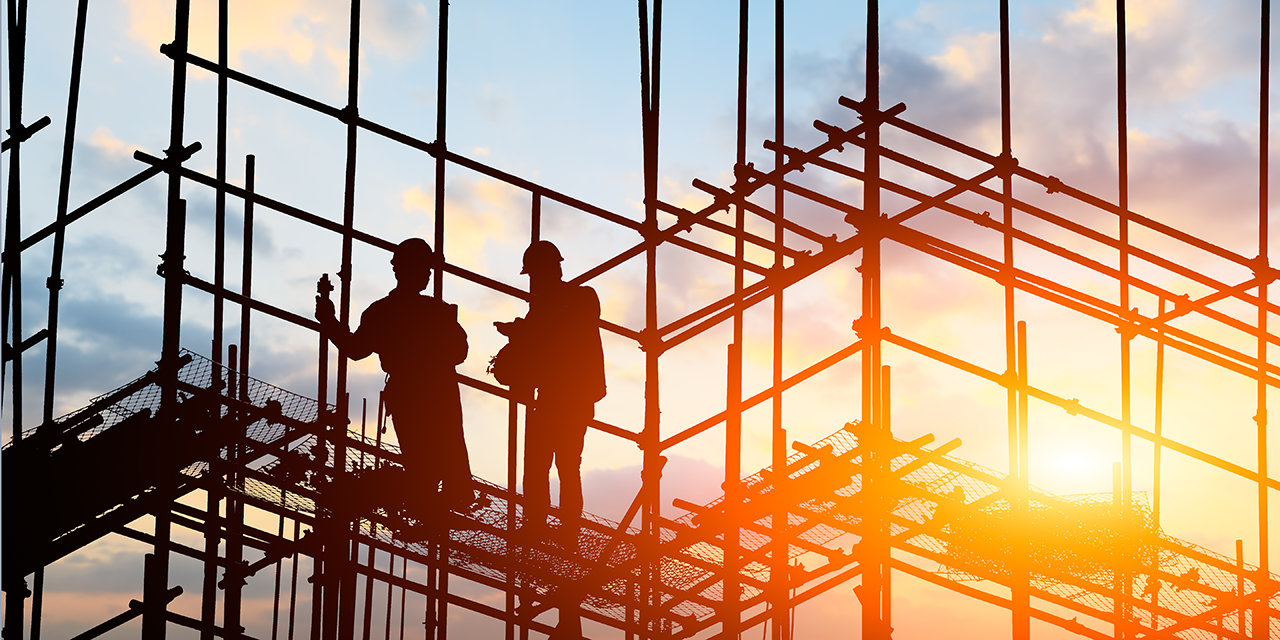 Two construction workings standing on scaffolding at sunrise