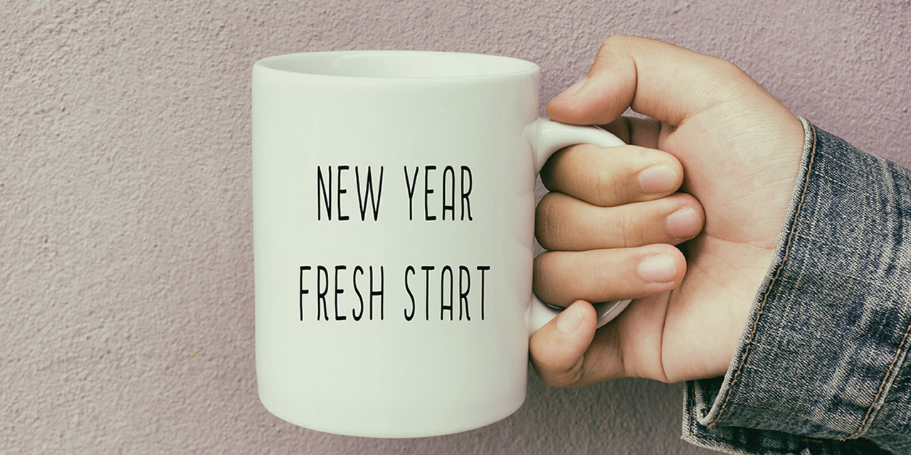 Hand holding a coffee mug with the words new year, fresh start printed on the cup.