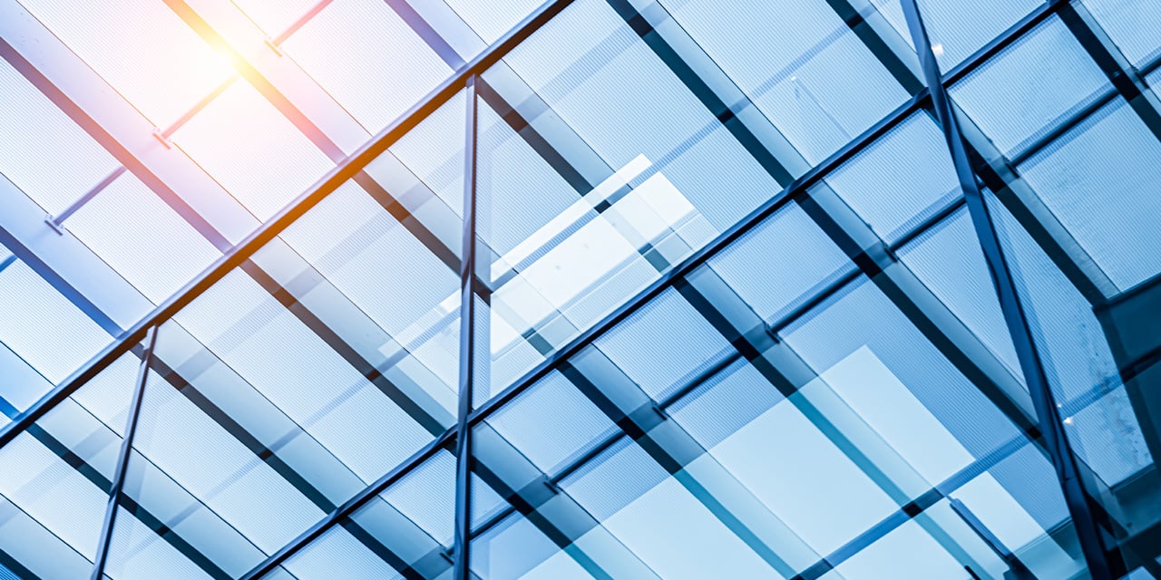 Glass building facade with intersecting reflective panels and sunlight shining through.