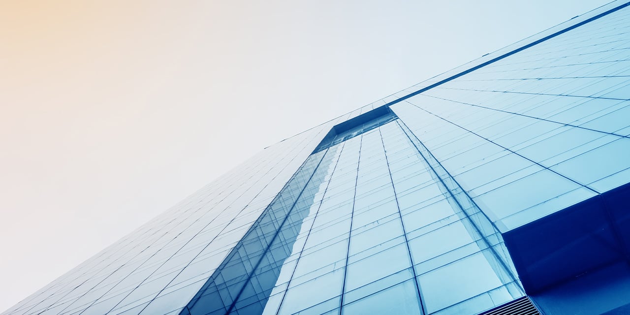 Upward view of a modern glass building reflecting soft sky tones with clean geometric lines.
