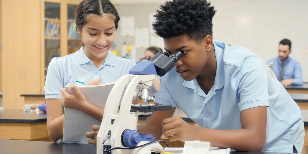 Two middle school students looking at a microscope and taking notes.