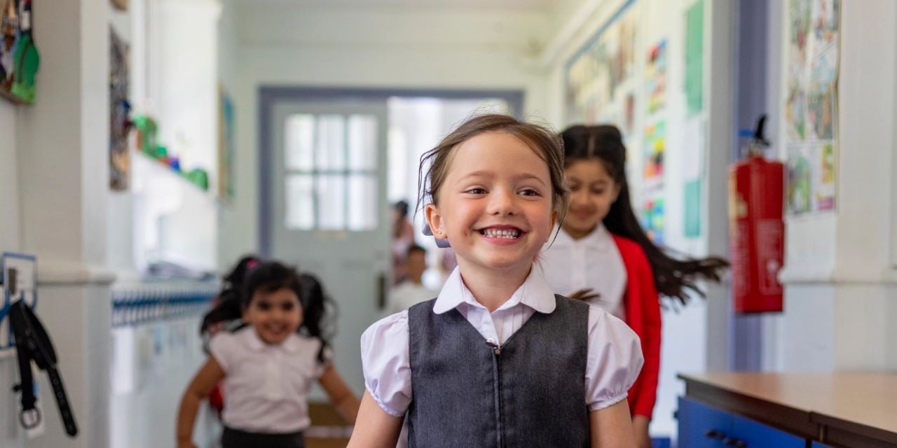 Elementary school aged students in uniforms walking down a school hallway.