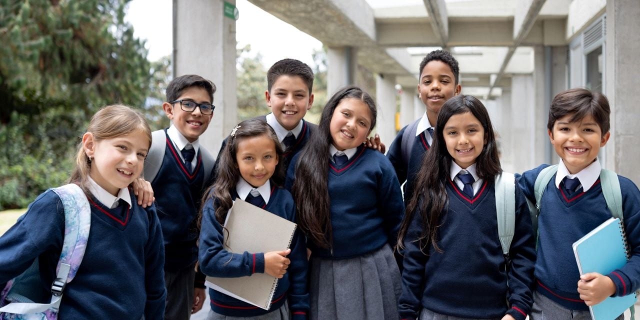 A group of students wearing uniforms standing outside of a school building.