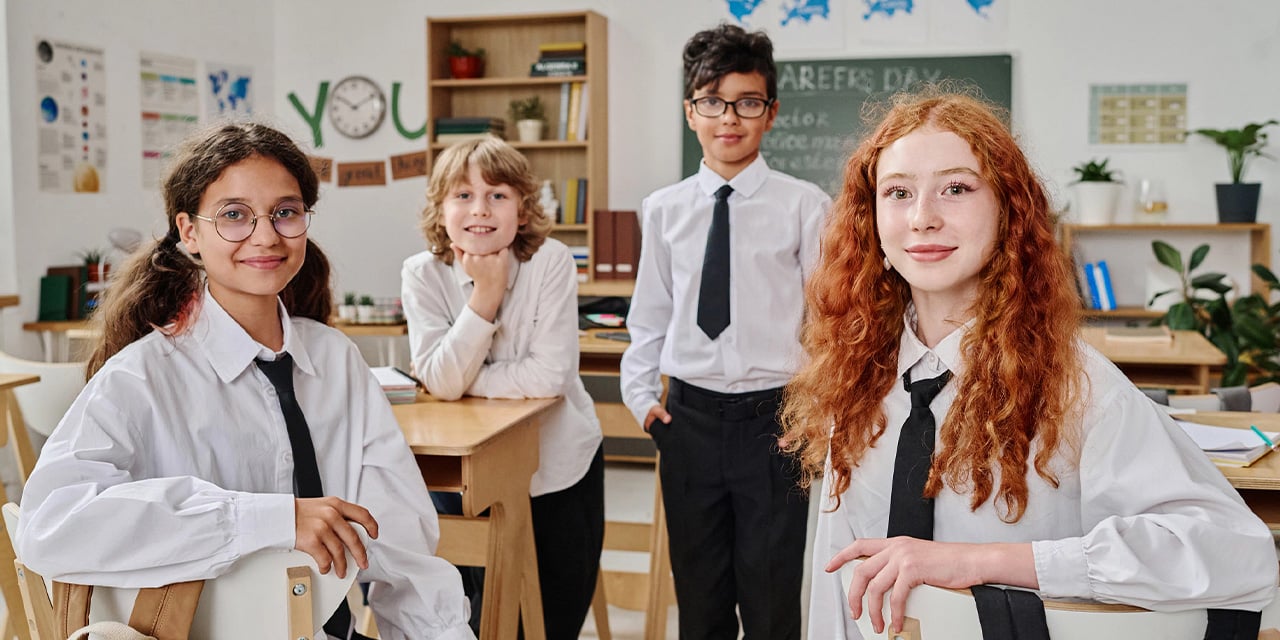 Four students wearing uniforms posing in a classroom.